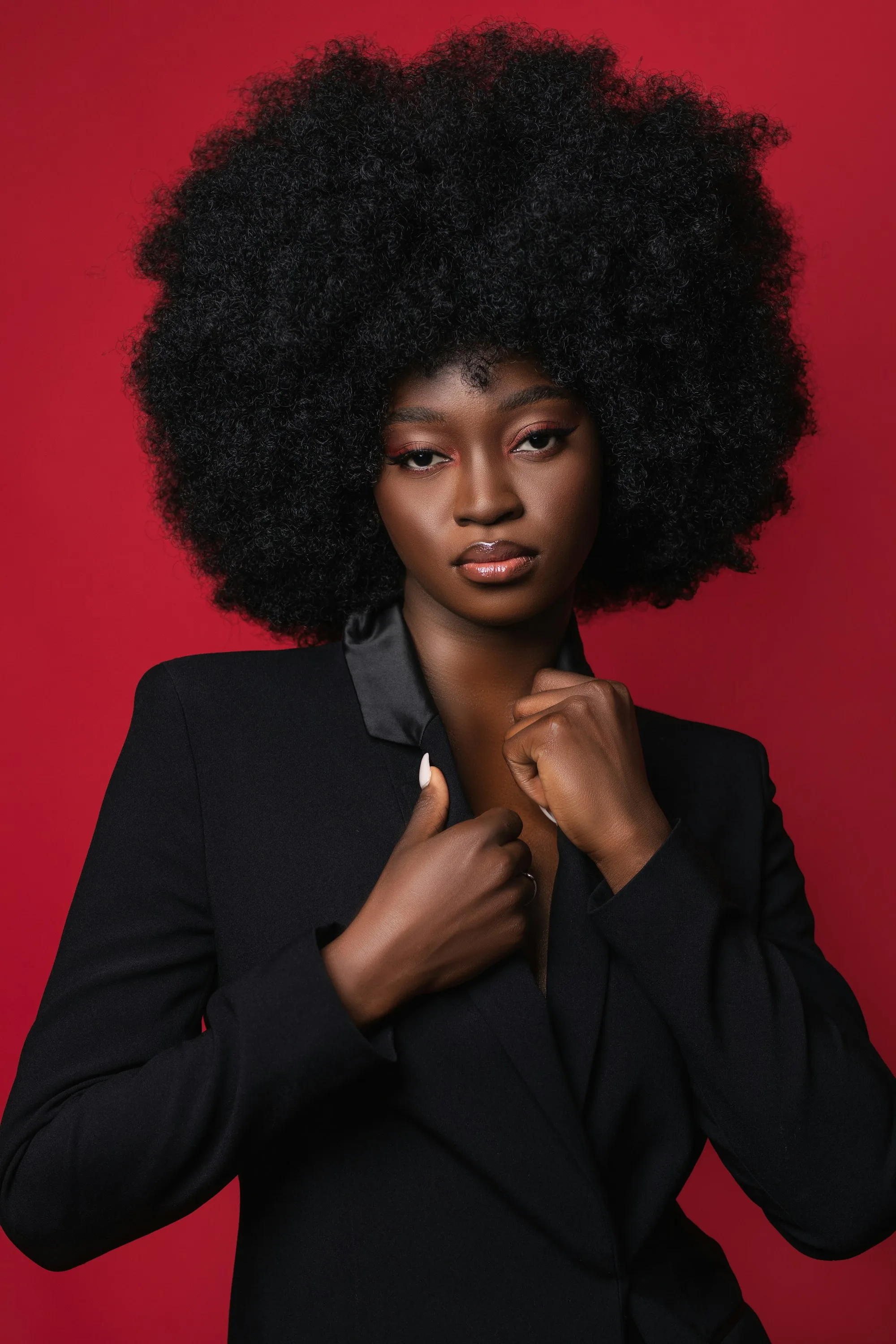 A model in a white cape blazer and wide trousers walks past photographers